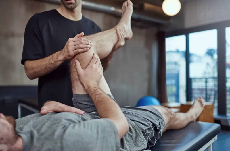 Fisioterapeuta realizando mobilização articular do joelho em paciente na maca
